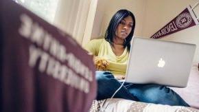 Student works on laptop on bed in dorm room